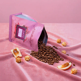 Open bag of coffee beans with scattered coffee beans and popcorn on a pink fabric background